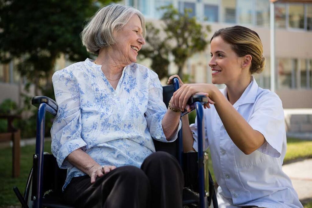 Older adult uses a hallway handrail while staff member checks an emergency call device nearby.